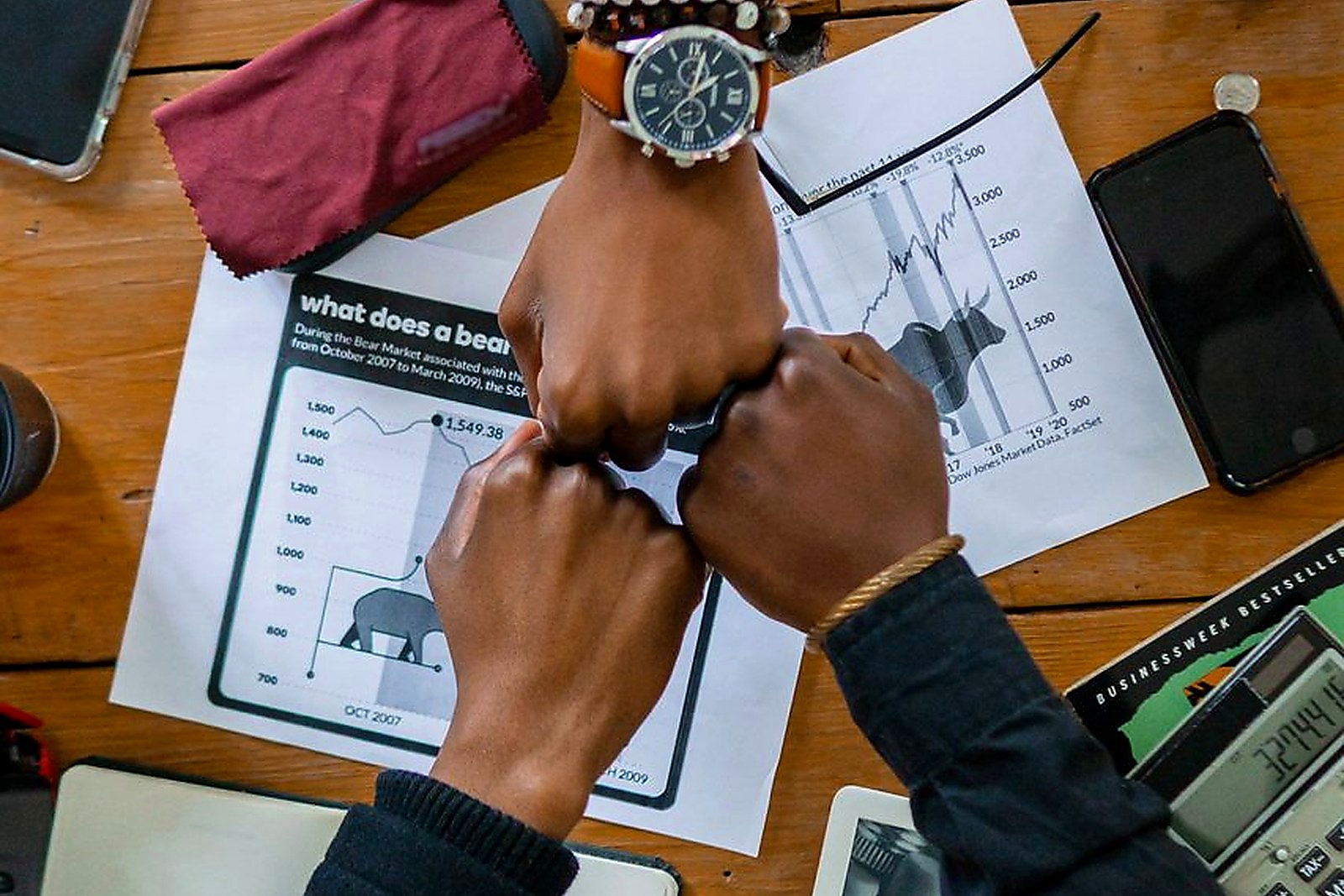 Free Coworkers joining fists over office desk, symbolizing teamwork and motivation. Stock Photo
